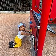 Thaysse participe au concours pour gagner de l'argent avec cette photo : toddler, child, playground, red, hat, yellow_pants, kneeling, outdoor, play_structure, toy, curious, fence, greenery, footwear, black_shoes, sunny, daylight, play, person, happy