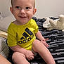 toddler, child, smile, yellow_shirt, adidas, bed, blanket, plush_toy, indoor, happy, person, barefoot, cute, infant, skin, face, legs, hand, sitting, cozy