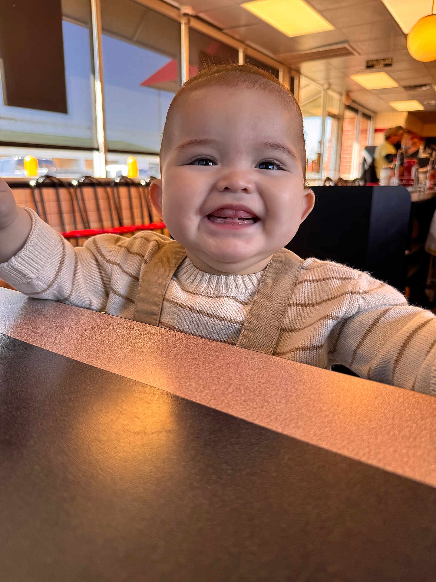Ethan joined the competition — help win amazing prizes! baby, smiling, child, indoor, restaurant, table, overalls, sweater, happy, face, person, dining, light, window, people, seat, furniture, casual, childhood, portrait