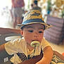 Thirdy is registered to the contest to win money with this photo: toddler, child, hat, pacifier, indoor, table, hand, face, curious, blurred_background, person, seated, clothing, short_sleeves, decor, furniture, pattern, expression, cute, young_child