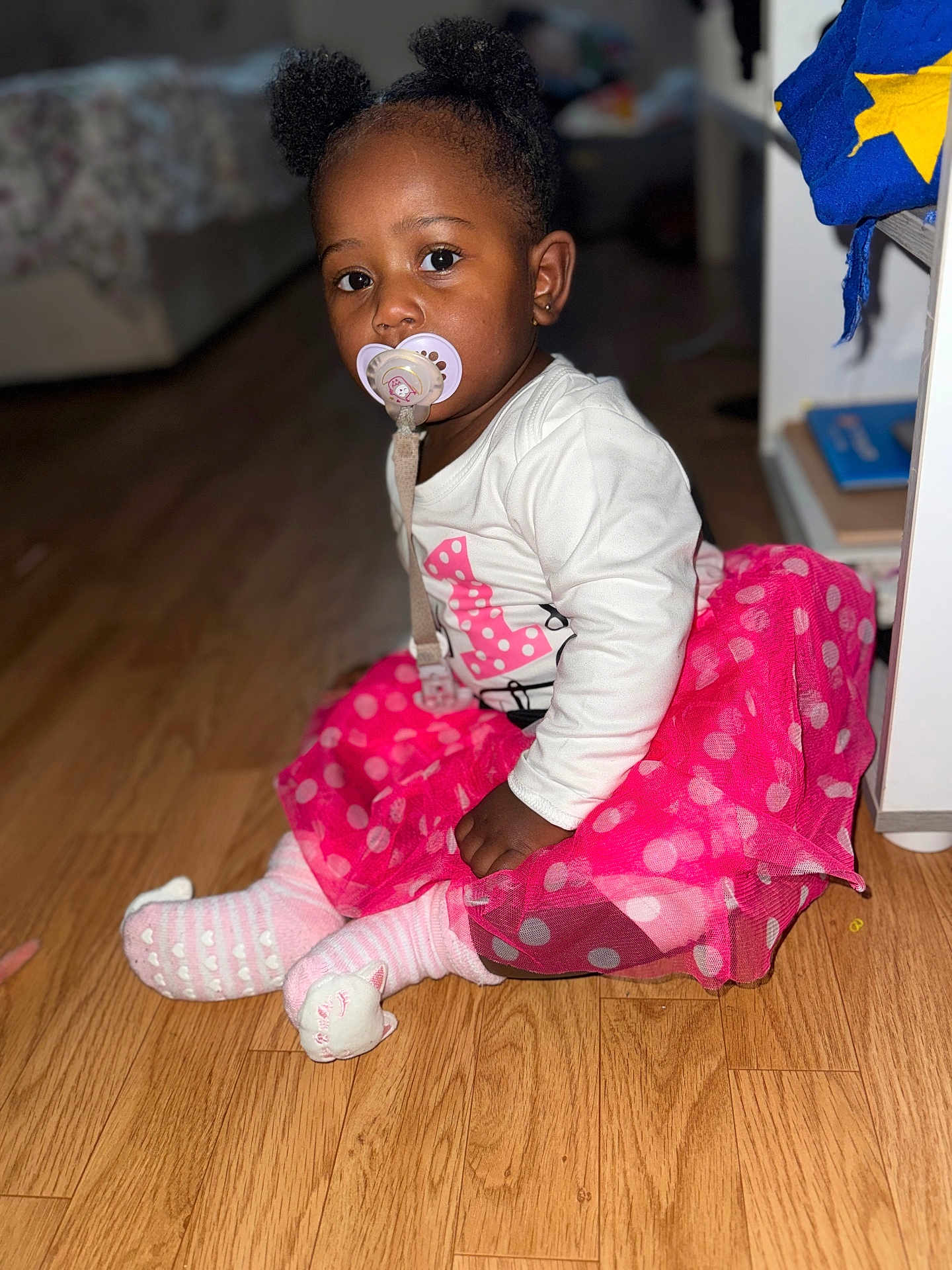 Larissa participe au concours pour gagner de l'argent avec cette photo : toddler, child, pacifier, pink_skirt, polka_dots, white_shirt, sitting, wooden_floor, indoor, cute, hair_puffs, socks, flooring, baby, portrait, young_child, clothing, earrings, focused, home