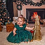 baby, child, dress, green_dress, smiling, sitting, christmas_tree, christmas_decorations, fireplace, teddy_bear, gift_boxes, golden_tree, holiday, festive, indoors, carpet, happy, cute, portrait, celebration