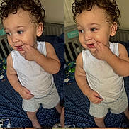 Karter is registered to the contest to win money with this photo: baby, bed, blue_bedspread, child, crib, curly_hair, cute, fingers_in_mouth, gray_shorts, home, indoor, person, playful, portrait, smiling, standing, toddler, two_images, white_tank_top, young_child