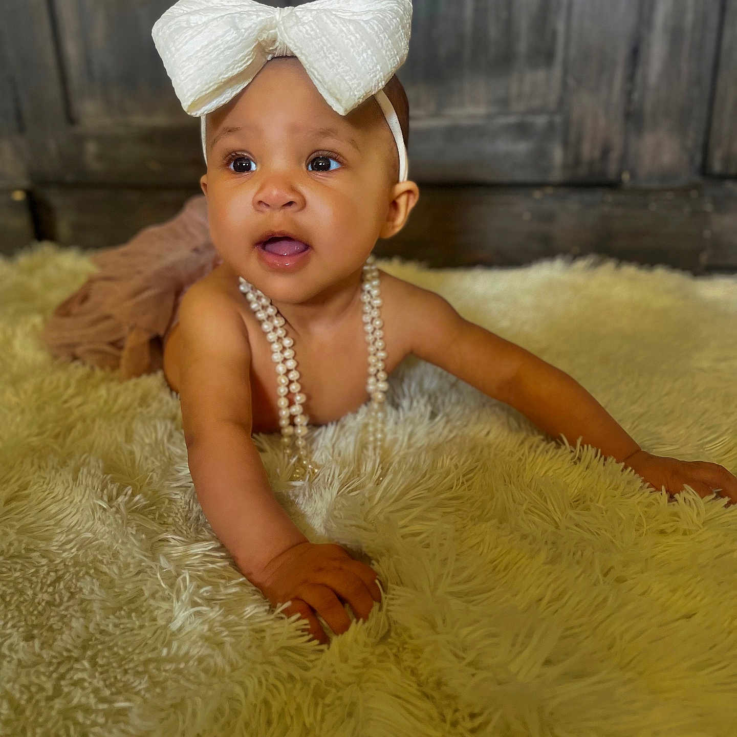 A Meyah joined the competition — help win amazing prizes! baby, bow, child, crawling, curious, cute, expression, floor, fluffy_rug, hand, headband, indoors, infant, pearl_necklace, portrait, skin, smiling, soft, wooden_background, young