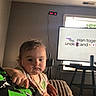 Emily is registered to the contest to win money with this photo: toddler, child, baby, portrait, indoors, sitting, pointing, serious, face, person, brown_hair, shirt, blanket, couch, television, presentation, screen, window, living_room, photograph