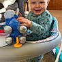 baby, child, smiling, pajamas, plush_toy, walker, indoor, carpet, furniture, living_room, toy, cute, standing, happy, person, footwear, animal_prints, cozy, home, infant