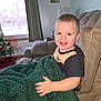 blanket, child, christmas_tree, couch, cozy, curtain, face, hand, happy, holiday_decor, indoor, lamp, living_room, pajamas, portrait, recliner, short_hair, smiling, toddler, window