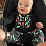 baby, baby_seat, blue_eyes, car_seat_style, carpet, child, chubby_cheeks, clothing, colorful_text, cute, happy, holiday_print, indoor, infant, let_it_glow, onesie, portrait, smiling, tiny_toes, wood_table