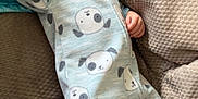 James is registered to the contest to win money with this photo: baby, sleeping, onesie, blue_clothing, dog_pattern, couch, beige, cozy, infant, hand, face, peaceful, resting, indoor, child, soft, textured, comfort, portrait, cute