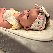 Kaycee joined the competition — help win amazing prizes! baby, infant, headband, smiling, lying_down, soft_blanket, cute, child, portrait, closeup, flower_pattern, clothing, indoors, happy, skin, face, young_child, baby_girl, head, apparel