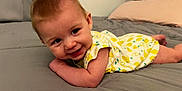 Kaycee joined the competition — help win amazing prizes! baby, infant, smile, bedroom, bed, blanket, clothing, yellow, white, lemon_print, cute, child, person, face, happy, skin, hair, toddler, resting, indoors
