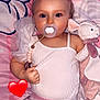 adorable, baby, blanket, child, clothing, cute, face, hand, heart_emoji, indoors, infant, lying_down, pacifier, pattern, pigtails, pink, sleepwear, soft_toy, stuffed_animal, toy