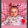 adorable, baby, blue_eyes, cat_pattern, child, closeup, clothing, cute, embroidery, face, heart_emoji, indoor, infant, lying_down, person, pigtails, pink_blanket, portrait, smiling, soft_lighting
