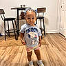 Kehlani is registered to the contest to win money with this photo: child, toddler, girl, standing, portrait, smiling, indoors, home, wood_floor, bar_stools, furniture, hair_bows, braids, snoopy_shirt, t_shirt, shorts, sneakers, houseplants, wall_art, hardwood_floor