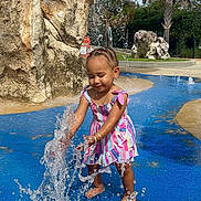 Kehlani is registered to the contest to win money with this photo: child, girl, toddler, outdoor, waterpark, fountain, water_splash, striped_dress, colorful_clothing, palm_tree, rock, waterfall, sunny, summer, barefoot, smiling, playing, portrait, pool, recreation