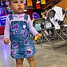 child, toddler, girl, portrait, standing, smiling, denim_dress, boots, braids, hair_accessories, k_pop, karaoke, music, stage, indoor, party, colorful_decorations, folding_chairs, snack, crowd