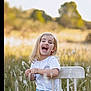 child, girl, laughing, white_chair, grass, field, outdoor, nature, sunlight, blonde_hair, casual_clothing, blue_jeans, white_shirt, happy, portrait, sitting, daylight, smile, greenery, trees