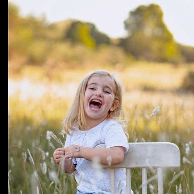 Sopho joined the competition — help win amazing prizes! blonde_hair, blue_jeans, casual_clothing, child, daylight, field, girl, grass, greenery, happy, laughing, nature, outdoor, portrait, sitting, smile, sunlight, trees, white_chair, white_shirt