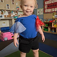 Camilla joined the competition — help win amazing prizes! toddler, child, indoor, playroom, blue_shirt, black_shorts, barefoot, curly_hair, smiling, educational_posters, toys, play_block, classroom, colorful, pumpkins, furniture, person, cute, happy, young_child