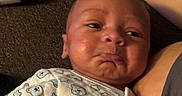 Amari is registered to the contest to win money with this photo: baby, infant, pout, onesie, bear_pattern, carpet, arm, bottle_cap, closeup, face, expression, cute, child, person, indoors, fabric, sleepwear, skin, newborn, lying_down