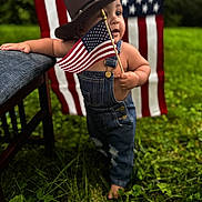 Amari joined the competition — help win amazing prizes! toddler, child, american_flag, cowboy_hat, denim_overalls, grass, outdoor, barefoot, chair, patriotic, flag, person, baby, portrait, summer, greenery, cute, standing, holiday, nature