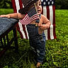 toddler, child, american_flag, cowboy_hat, denim_overalls, grass, outdoor, barefoot, chair, patriotic, flag, person, baby, portrait, summer, greenery, cute, standing, holiday, nature