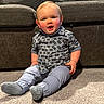 Riley is registered to the contest to win money with this photo: baby, child, infant, sitting, smiling, happy, portrait, indoor, couch, carpet, plaid_shirt, trousers, socks, clothing, face, eyes, mouth, home, furniture, sunlight