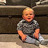 baby, child, infant, smiling, sitting, portrait, indoor, living_room, couch, carpet, plaid_shirt, pants, socks, rosy_cheeks, blond_hair, happy, family_photo, furniture, home, photography