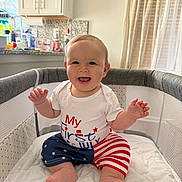 Riley joined the competition — help win amazing prizes! baby, child, infant, smiling, happy, sitting, playpen, indoor, kitchen, home, portrait, white_shirt, patriotic_clothing, star_pattern, striped_clothing, bare_feet, hands, curtains, sunlight, family_photo