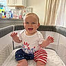 baby, child, infant, smiling, happy, sitting, playpen, indoor, kitchen, home, portrait, white_shirt, patriotic_clothing, star_pattern, striped_clothing, bare_feet, hands, curtains, sunlight, family_photo