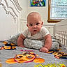 baby, infant, child, portrait, tummy_time, lying_down, sitting, face, eyes, gray_shirt, bedroom, bed, blanket, pillow, stuffed_animal, paw_patrol, cartoon, window, indoor, smiling