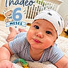 baby, child, infant, portrait, smiling, happy, indoor, nursery, crib, blanket, bandana, striped_clothing, toy, teething_toy, lying_down, face, eyes, adorable, six_months, text_overlay