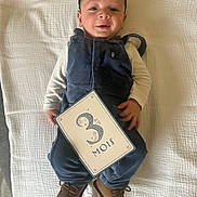 Atlas a rejoint le concours — aidez-le/la à gagner de superbes lots ! baby, infant, smiling, blue_overalls, brown_shoes, white_blanket, card, 3_months, lying_down, cute, child, portrait, indoors, happy, young_child, clothing, hand, face, head, feet