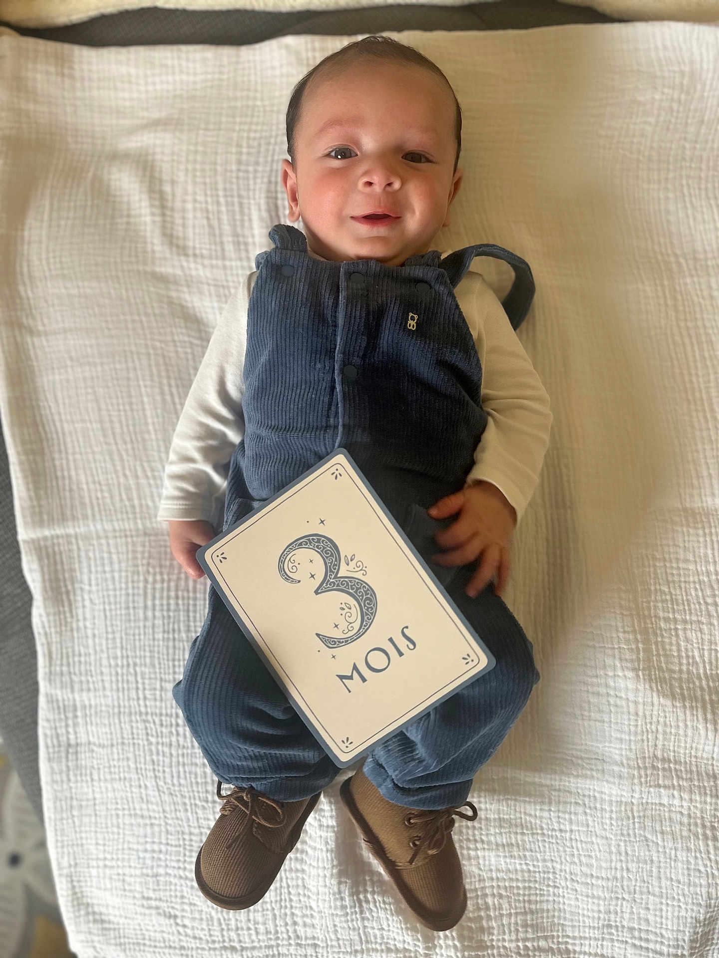 Atlas a rejoint le concours — aidez-le/la à gagner de superbes lots ! baby, infant, smiling, blue_overalls, brown_shoes, white_blanket, card, 3_months, lying_down, cute, child, portrait, indoors, happy, young_child, clothing, hand, face, head, feet