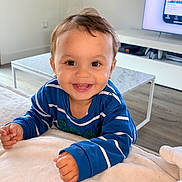 Hugo a rejoint le concours — aidez-le/la à gagner de superbes lots ! blanket, blue_sweater, child, cute, face, floor, furniture, hands, happy, home, indoor, living_room, modern, person, smiling, striped_clothing, table, television, toddler, wood_floor