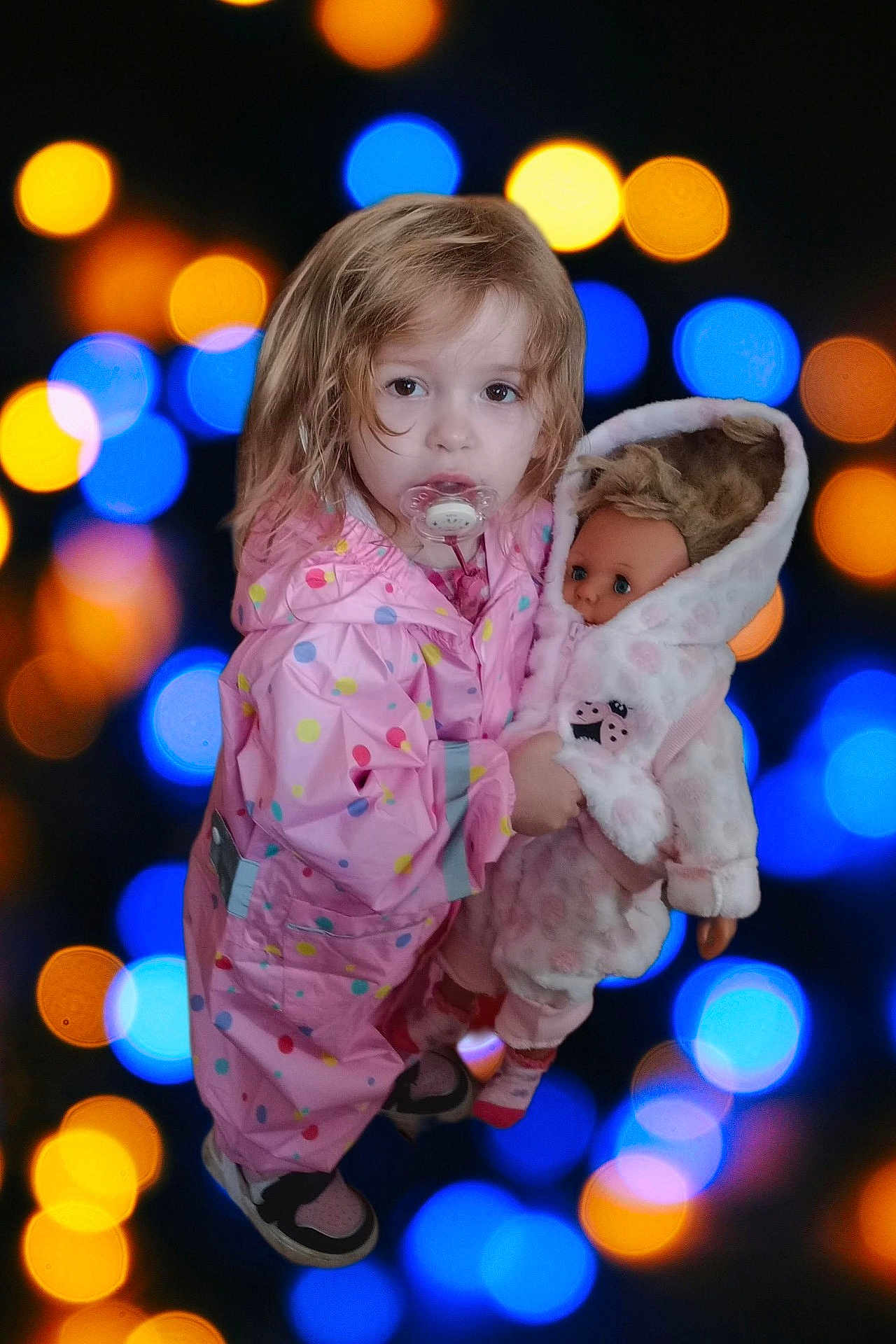 Laura participe au concours pour gagner de l'argent avec cette photo : child, toddler, raincoat, pink, polka_dot, doll, toy, pacifier, face, hair, bokeh, lights, blue, orange, clothing, footwear, indoor, portrait, cute, holding