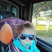 Mathis participe au concours pour gagner de l'argent avec cette photo : child, toddler, sunglasses, pacifier, car_seat, seatbelt, blue_jacket, window, car_interior, road_sign, tree, sunlight, outdoor, road, transport, seat, person, baby, portrait, daytime