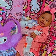 Mahari is registered to the contest to win money with this photo: baby, child, pink, hello_kitty, plush_toy, blanket, pajamas, smiling, bow, cute, indoors, toy, colorful, soft_toy, patterned_blanket, happy, sitting, childrens_clothing, playful, cozy