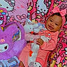 baby, child, pink, hello_kitty, plush_toy, blanket, pajamas, smiling, bow, cute, indoors, toy, colorful, soft_toy, patterned_blanket, happy, sitting, childrens_clothing, playful, cozy