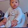 Mahari is registered to the contest to win money with this photo: baby, child, infant, white_clothing, gold_jewelry, hair_bows, baby_seat, indoor, poster, hello_kitty, curious, calm, face, hand, foot, sitting, cute, childrens_room, soft_lighting, portrait