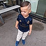 Lisandro participe au concours pour gagner de l'argent avec cette photo : child, boy, standing, outdoor, concrete, picnic_table, glass_window, real_madrid_jersey, sportswear, sneakers, hairstyle, curious_expression, casual_clothing, side_view, urban, daylight, young, person, fashion, street