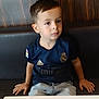 child, boy, sitting, table, restaurant, booth, casual_clothing, jeans, short_hair, indoor, portrait, looking_away, navy_jersey, sportswear, adidas_logo, real_madrid_jersey, hands_on_bench, wood_paneling, young_person, calm_expression