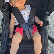 Tahyra a rejoint le concours — aidez-le/la à gagner de superbes lots ! baby, child, stroller, headband, pink_sandals, white_shirt, red_shorts, outdoor, sunlight, curious_expression, seatbelt, baby_clothing, footwear, baby_girl, infant, black_stroller, daylight, summer, cute, portrait