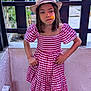 Lorena participe au concours pour gagner de l'argent avec cette photo : casual_clothing, checkered, child, dress, fence, flower, garden, girl, hands_on_hips, hat, headwear, nature, outdoor, person, portrait, red_and_white, serious_expression, standing, summer, young