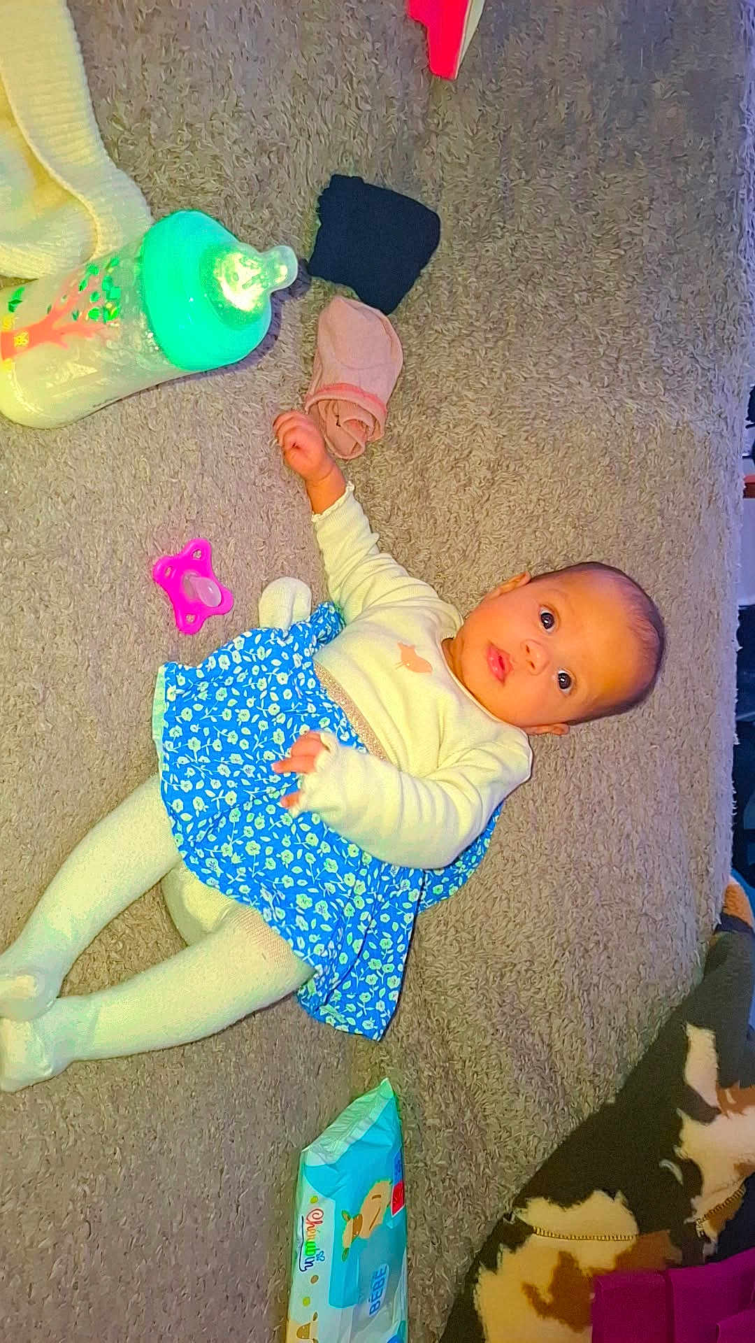 Keya participe au concours pour gagner de l'argent avec cette photo : baby, infant, carpet, bottle, pacifier, baby_wipes, blue_skirt, white_top, tights, face, person, child, lying_down, indoors, cute, clothing, floor, toy, blanket, expression