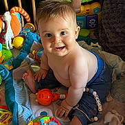 Tiago participe au concours pour gagner de l'argent avec cette photo : baby, bare_chest, blanket, child, colorful, cute, face, foot, hand, happy, indoor, infant, pants, person, playmat, plush, rattle, sitting, smiling, toy