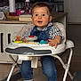 baby, walker, denim_overalls, checkered_shirt, toy, happy, smiling, indoor, floor, feet, child, face, person, home, cabinet, table, jar, spray_bottle, wood_floor, footwear
