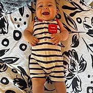 Tiago participe au concours pour gagner de l'argent avec cette photo : baby, child, smiling, striped_clothing, romper, blanket, pattern, pillow, happy, infant, indoor, cute, person, face, legs, hands, skin, lying_down, summer, text_patch