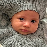 Isabella is registered to the contest to win money with this photo: baby, infant, child, portrait, face, eyes, smiling, knitted_clothing, wool, hat, pom_pom, gray, cozy, blanket, indoor, close_up, sitting, fashion, cute, photography