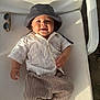 baby, bucket_hat, casual, chair, child, cute, embroidery, footwear, happy, hat, infant, outdoor, portrait, relaxing, shirt, smiling, striped_pants, sunglasses, sunlight, white_chair